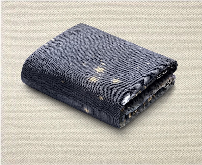 May include: Folded navy blue fabric with a constellation pattern featuring gold stars and white dots. The fabric is folded neatly, showcasing the design on the top layer. The fabric is likely a textile, possibly for crafting or home decor.