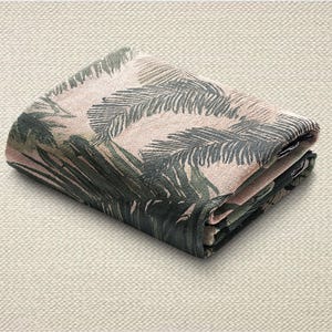 May include: Folded fabric with a tropical leaf design in green and pink hues. The textile is neatly folded, displaying the intricate pattern. The background is a neutral, textured surface.
