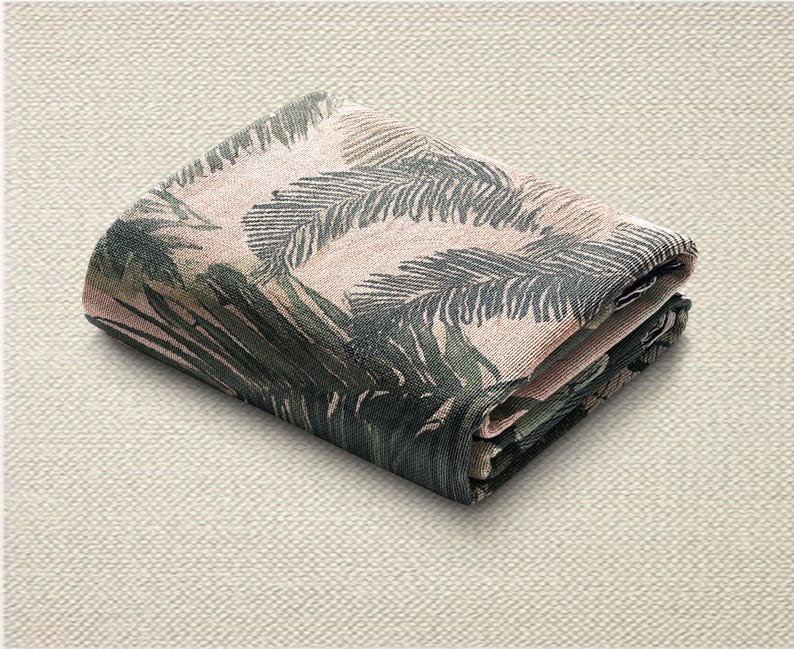 May include: Folded fabric with a tropical leaf design in green and pink hues. The textile is neatly folded, displaying the intricate pattern. The background is a neutral, textured surface.