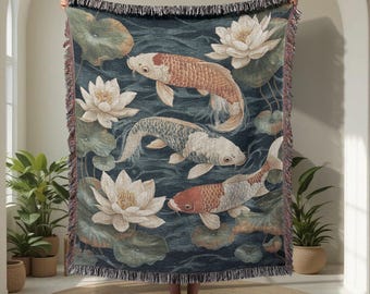May include: A woven throw blanket featuring a koi pond design. The blanket displays koi fish in shades of orange, white, and gray, swimming among lily pads and lotus flowers. The background is a dark teal color. The blanket has a fringed edge.