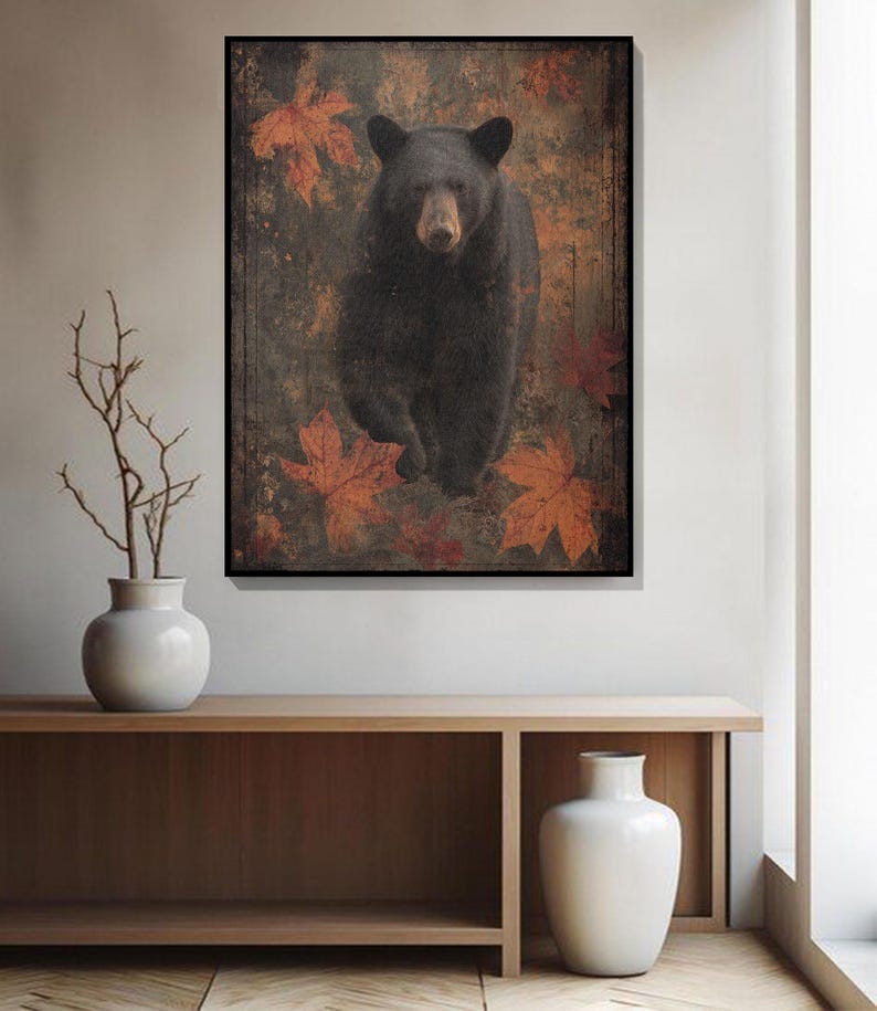 May include: A framed art print featuring a black bear walking forward, set against a backdrop of autumn leaves. The bear has dark fur and a light brown snout. The leaves are shades of orange and red, creating a rustic, nature-inspired aesthetic.