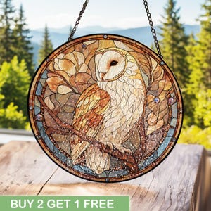 Puede incluir: Ventana redonda de vidrieras con un búho común posado en una rama. El búho tiene plumas blancas y marrones, con un diseño detallado de vidrieras. La ventana tiene un borde marrón oscuro y cuelga de una cadena.