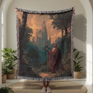 Puede incluir: Una manta tejida con un tapiz que presenta una escena de fantasía con un mago con túnica y sombrero rojos, sosteniendo un bastón, frente a un castillo. La obra de arte tiene una estética vintage con un bosque y un atardecer de fondo.