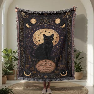 Può includere: Una coperta tessuta che raffigura un gatto nero seduto davanti a una grande luna. Il design include un pentagramma, fasi lunari e un layout da tavola spiritica con l'alfabeto e la parola GOODBYE. La coperta presenta bordi sfrangiati.