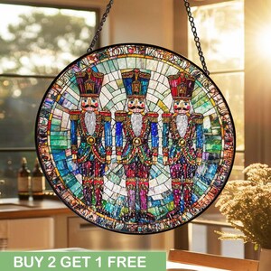 May include: A round stained glass window featuring three colorful nutcracker soldiers. The soldiers wear blue, red, and gold uniforms with white beards. The background is a mosaic of blues, greens, and yellows. The text "BUY 2 GET 1 FREE" is at the bottom.