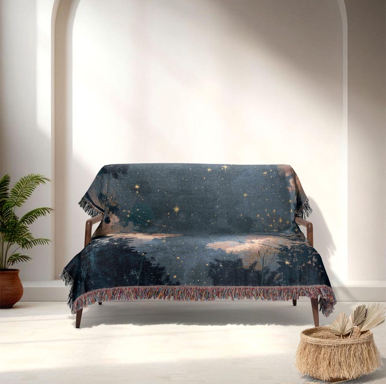 May include: A dark blue throw blanket with a celestial design featuring stars and a forest scene. The blanket is draped over a wooden sofa and has a fringed edge. The colour palette includes shades of blue, gold, and brown.