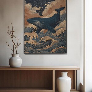 May include: A framed art print depicts a dark blue whale leaping above stylized ocean waves. The artwork features a starry sky, clouds, and gold accents, creating a serene and artistic scene. The print is displayed on a wooden console.