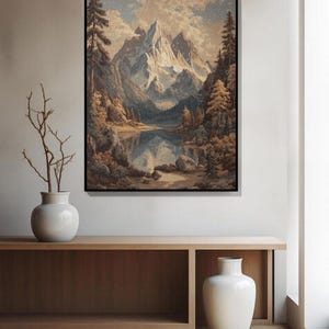 May include: A framed landscape painting depicts a mountain range with snow-capped peaks reflected in a calm lake. The artwork features a color palette of blues, browns, and greens, with trees and clouds adding depth. The painting is displayed above a wooden console.