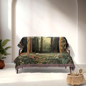 May include: A tapestry throw blanket draped over a wooden sofa. The blanket features a detailed forest scene with trees, foliage, and flowers in shades of green, brown, and red. The blanket has a fringed edge.