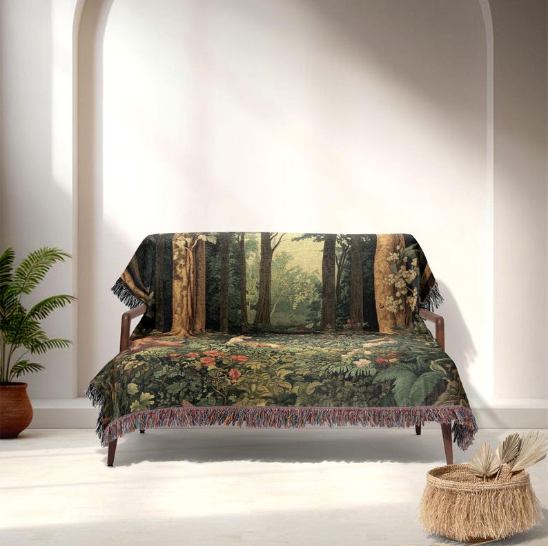 May include: A tapestry throw blanket draped over a wooden sofa. The blanket features a detailed forest scene with trees, foliage, and flowers in shades of green, brown, and red. The blanket has a fringed edge.