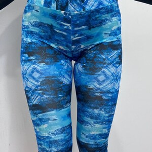 Może przedstawiać: Legginsy capri we wzór w kolorze niebieskim i czarnym. Legginsy mają wysoki stan i żywy, abstrakcyjny wzór. Paleta kolorów obejmuje odcienie niebieskiego i czarnego, tworząc dynamiczny efekt wizualny. Legginsy są do kolan.