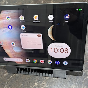May include: A black tablet displaying a Jupiter-themed wallpaper and app icons. The screen shows the time as 10:08 AM on Saturday, October 25. The tablet is propped up on a gray stand.
