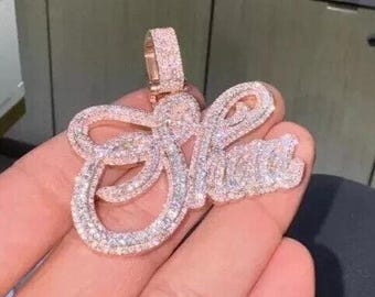May include: A rose gold pendant spelling out the name "Shine" in a cursive font. The pendant is encrusted with small, sparkling stones. The bail is also rose gold and covered in stones. The pendant is held in a hand.