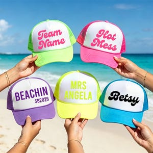 Puede incluir: Cinco gorras de camionero coloridas, con frentes blancos y respaldos de malla, se muestran sobre un fondo de playa. Cada gorra tiene un esquema de color diferente y el texto: "Team Name", "Hot Mess", "Beachin SB2026", "Mrs Angela" y "Betsy".