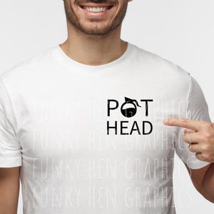 May include: White t-shirt with the words "POT HEAD" in black, featuring a coffee pot graphic. The person is pointing at the shirt. The shirt is a crew neck style.