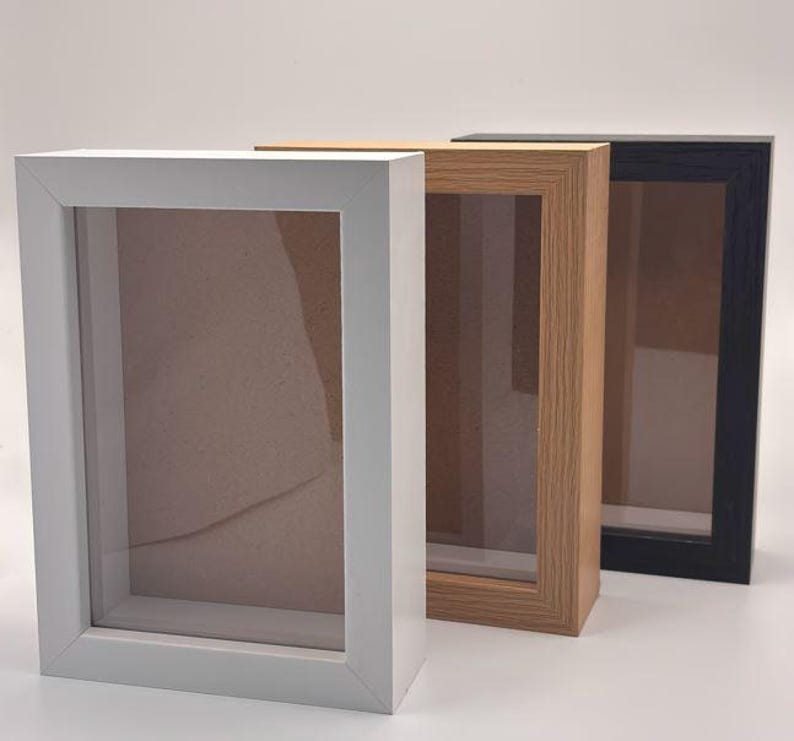 Pode incluir: Tr&ecirc;s molduras de caixa de sombra em branco, madeira natural e preto. Cada moldura tem formato retangular com frente de vidro e interior rebaixado. As molduras s&atilde;o projetadas para exibir itens e criar um efeito 3D.