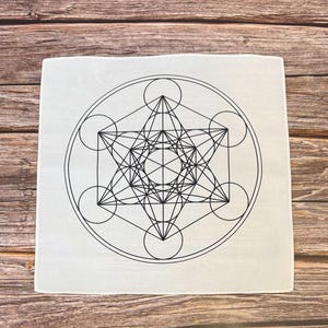 May include: Square, off-white cloth featuring a black Metatron's Cube design. The geometric pattern includes interconnected circles, lines, and a central star shape. The cloth is likely used for spiritual or decorative purposes.
