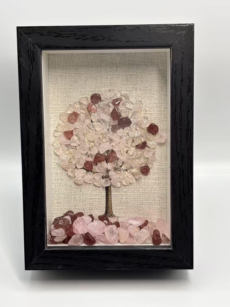 Pode incluir: Uma obra de arte emoldurada com uma &aacute;rvore feita de pedras preciosas rosa e claras. A &aacute;rvore tem um tronco marrom e uma copa de pedras rosa claro e vermelhas, contra um fundo de tecido neutro. A moldura &eacute; preta.