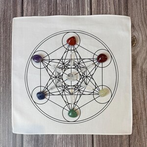 May include: White square cloth with a black geometric design featuring circles, lines, and a star-like shape. The design is surrounded by seven colorful gemstones: red, purple, red, yellow, green, blue, and clear quartz crystals.