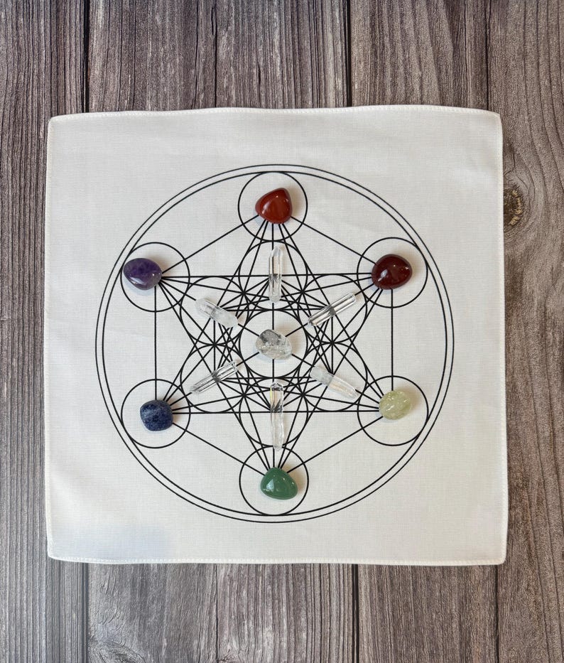 May include: White square cloth with a black geometric design featuring circles, lines, and a star-like shape. The design is surrounded by seven colorful gemstones: red, purple, red, yellow, green, blue, and clear quartz crystals.