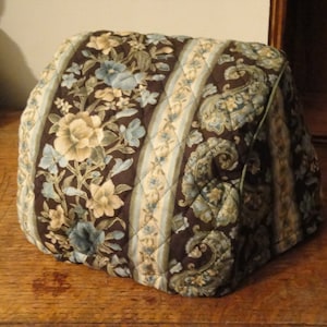 May include: A brown quilted fabric cover with a blue and white floral pattern. The cover has a quilted diamond pattern and is designed to fit a kitchen appliance.