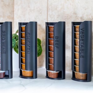 May include: Four black, vertical food storage containers labelled "Red Wine", "Chicken", "Beef", and "Vegetable". Each container holds multiple small, individual servings of food or drink. The containers are on a light-coloured surface.