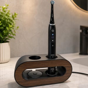 May include: A black Oral-B iO electric toothbrush standing in a horizontal, oval-shaped charging dock with a dark wood grain finish. The toothbrush handle features a digital display screen showing a tooth icon and the text 0:00.