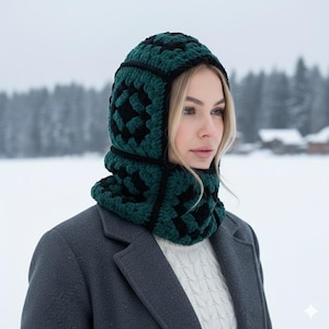 May include: A green and black crochet balaclava with a geometric pattern. The balaclava covers the head and neck, providing warmth. The balaclava is made of a soft, textured yarn. The background is a snowy landscape with trees.