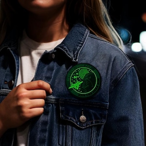 May include: A circular green patch with the text "ACFT LAG - 90TH FGS" and "JOIN THE DARK SIDE" on a denim jacket. The patch features a green illustration of a spaceship and Darth Vader.