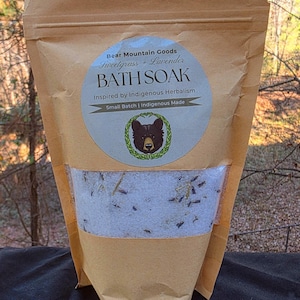May include: A brown paper bag of Bear Mountain Goods Bath Soak. The label reads "Sweetgrass + Lavender" and "Inspired by Indigenous Herbalism." The bag has a clear window showing the bath soak with lavender and other herbs.