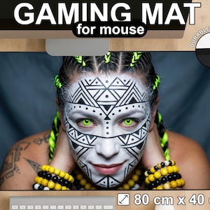 Könnte beinhalten: Gaming-Mauspad mit auffälligem Design. Das Pad zeigt ein Porträt mit Stammes-Gesichtsbemalung, grünen Augen und gelb-schwarzen Accessoires. Das Pad misst 80 cm x 40 cm.