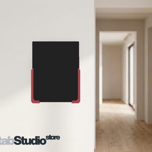 May include: A rectangular black tablet or display screen mounted on a wall, featuring a dark central panel framed by two distinct, angular red corner brackets at the bottom left and right sides, providing a secure and minimalist mounting structure.