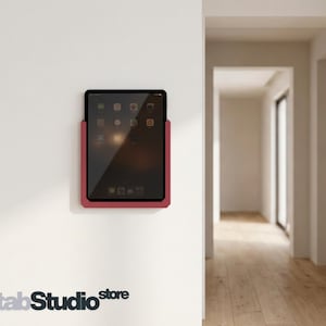 May include: A dark red tablet wall mount holding a black tablet with a visible screen interface. The mount is secured to a plain white wall. The text tabStudio store is printed in dark grey at the bottom left corner of the image.