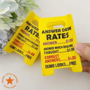 May include: Two yellow plastic signs with the text "ANSWER DESK RATES" and a list of prices for different types of answers. The signs are in a stand-up design with a handle at the top.