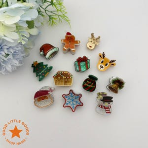 Könnte beinhalten: Eine Sammlung von dekorativen Anstecknadeln zum Thema Weihnachten. Die Anstecknadeln zeigen einen Weihnachtsmann, einen Lebkuchenmann, einen Weihnachtsbaum, ein Rentier, ein Geschenk, ein Haus, einen Schneeflocke, eine Glocke und einen Schneemann. Die Anstecknadeln sind farbenfroh.