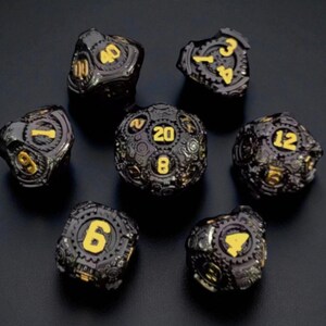 May include: Set of seven black and gold dice with a steampunk design. Each die features gold numbers and intricate gear-like detailing. The dice are arranged on a dark surface, showcasing their unique aesthetic.
