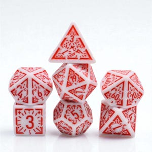 Puede incluir: Un conjunto de siete dados poliédricos blancos con números y diseños rojos. El conjunto incluye un d4, d6, d8, d10, d12, d20 y un dado de porcentaje, ideal para juegos de rol.