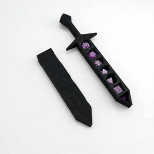 Puede incluir: Soporte negro en forma de espada para dados con una funda a juego. La espada contiene varios dados morados. El diseño es angular y geométrico, con un tema de fantasía. Los dados son visibles en los compartimentos de la espada.