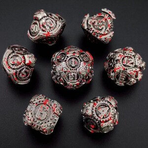 May include: Set of seven metallic dice with a steampunk aesthetic. The dice are silver with red accents and feature intricate gear and cog designs. Numbers are displayed in a stylized font.