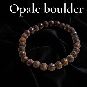 Peut inclure: Un bracelet composé de perles de opale boulder marron et beige. Les perles rondes sont enfilées ensemble, formant une forme circulaire. Le texte "Opale boulder" est affiché en blanc en haut de l'image.