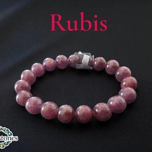 Op de afbeelding: Een Rubis armband met grote, ronde, roze-rode kralen. De armband heeft een zilverkleurige sluiting. Het woord "Rubis" staat in roze tekst boven de armband. Het Legendstones-logo staat linksonder.