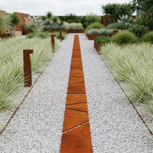 Peut inclure: Un chemin de jardin paysager avec une rangée centrale de dalles géométriques de couleur rouille. Le chemin est bordé de gravier gris clair et de graminées ornementales. Des luminaires rectangulaires bruns sont espacés le long du chemin, avec diverses plantes et arbustes en arrière-plan.