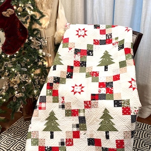 May include: A Christmas-themed quilt with a white background, featuring red, green, and black squares, along with green Christmas trees and red star designs. The quilt has a red and green border with a black and white striped edge.