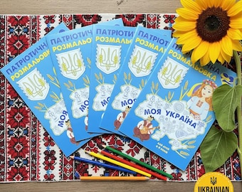 May include: A collection of blue coloring books featuring Ukrainian text and illustrations, including the Ukrainian coat of arms and a map. The books are displayed with coloured pencils and a sunflower. The text on the book reads "My Ukraine".