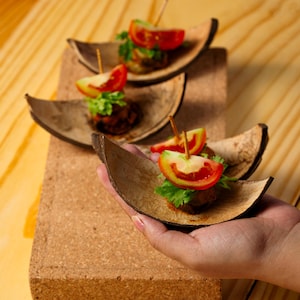 May include: Small appetisers served in curved, brown, natural fibre bowls. Each portion features a dark, cooked base topped with a fresh green herb sprig and a bright red tomato wedge, all secured with a thin wooden toothpick for easy handling.