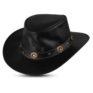 Peut inclure: Chapeau de cowboy en cuir noir avec un large bord et une bande décorative. La bande présente des médaillons et des rivets en métal en relief. Le chapeau a un style western classique.