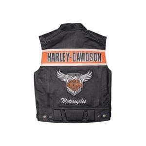 Può includere: Un gilet in pelle nera con una striscia orizzontale arancione sulla parte superiore della schiena con il testo HARLEY-DAVIDSON. Sotto, una toppa con emblema alato mostra il testo MOTOR HARLEY-DAVIDSON CYCLES 115, con la parola Motorcycles.