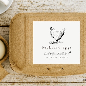 May include: A cardboard egg carton with a white label featuring a black and white illustration of a hen. The label reads "backyard eggs, hand gathered with love, SMITH FAMILY COOP". A few eggs are visible.
