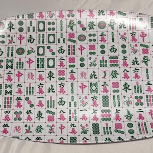 May include: White, oval-shaped serving platter with a repeating pattern of Mahjong tiles in green and pink. The tiles feature various symbols and Chinese characters, creating a decorative and thematic design.