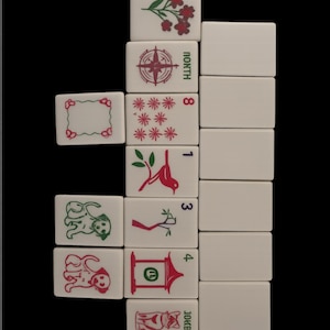 May include: A collection of white Mahjong tiles with various red and green symbols and numbers. The tiles feature images of flowers, a compass, stars, birds, and dogs. The word "NORTH" is visible on one tile, and "JOKER" on another.